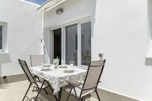 An outdoor dining area with a table set for two, chairs, and a window with blinds.