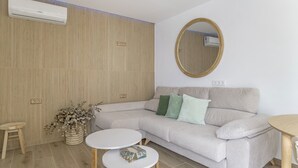 Una sala moderna con un sofá color beige, dos mesas redondas, piso de madera y aire acondicionado instalado en la pared.