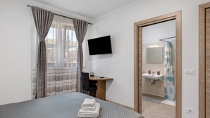 Habitación de hotel con cama, escritorio, televisión, baño con lavabo y espejo, y ducha.
