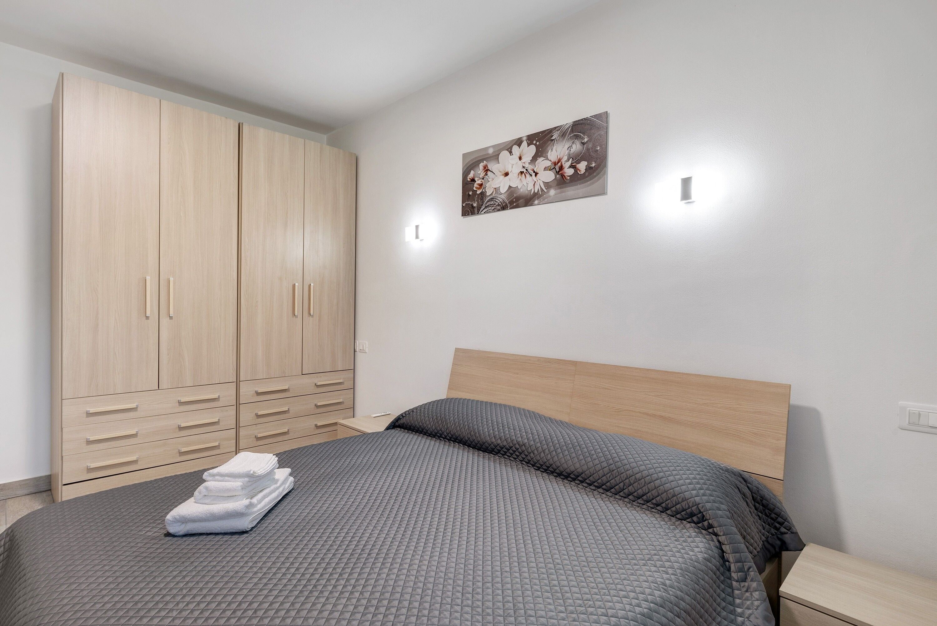 Une chambre à coucher avec un lit, une armoire et une lampe fixée au mur.