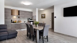 A modern kitchen with grey cabinets, a dining table with chairs, and a flat-screen TV mounted on the wall.