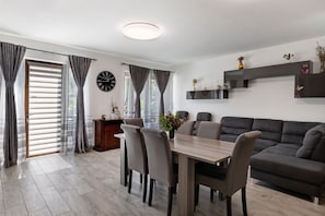 Un salon moderne comprenant une table à manger, des chaises, un canapé, une horloge et une cheminée.