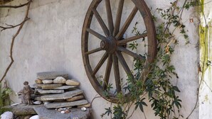 A rustic stone wall with a large wooden wheel, a stack of flat stones, and a small figurine.