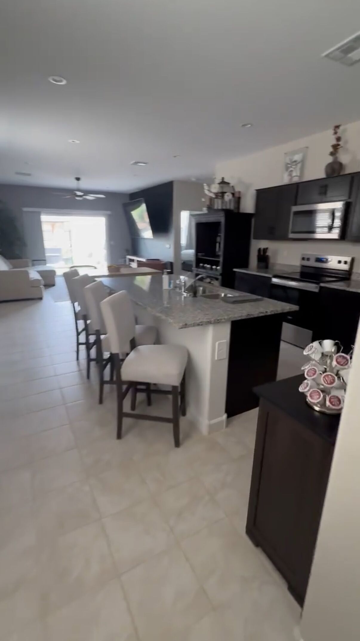 A modern kitchen with a central island, bar stools, dark cabinetry, and a microwave.