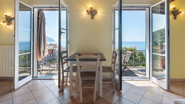 A room with a table and chairs, a sliding glass door leading to a balcony with a view of the sea. - Apartment 'Le Pale - Girasole' with Sea View, Wi-Fi and Air Conditioning (Bogliasco)