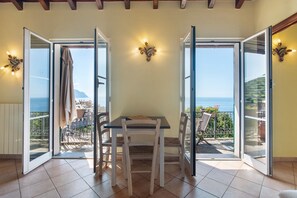 Ein Zimmer mit Tisch und Stühlen, eine Glastür mit Schieberiegel und Zugang zu einem Balkon mit Meerblick.