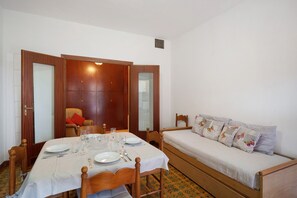 Quarto com mesa de jantar posta para quatro, sofá com almofadas estampadas e guarda-roupa de madeira.