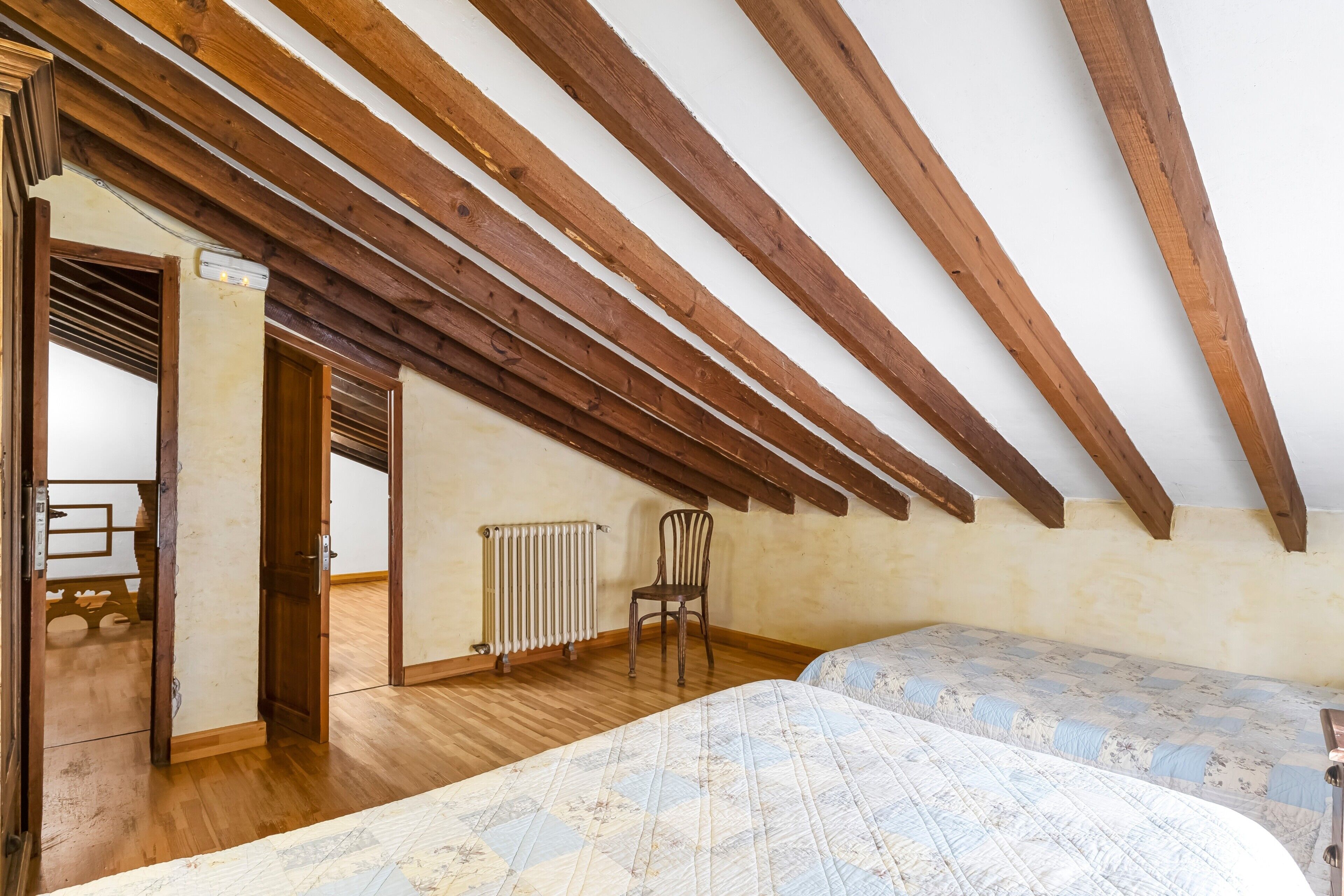 Ein Zimmer mit Holzbalken, einem Heizkörper, einem Sessel und zwei Betten mit gemusterten Laken.