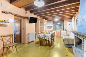 A rustic interior with a wooden dining table, chairs, a fireplace, and a kitchen area.