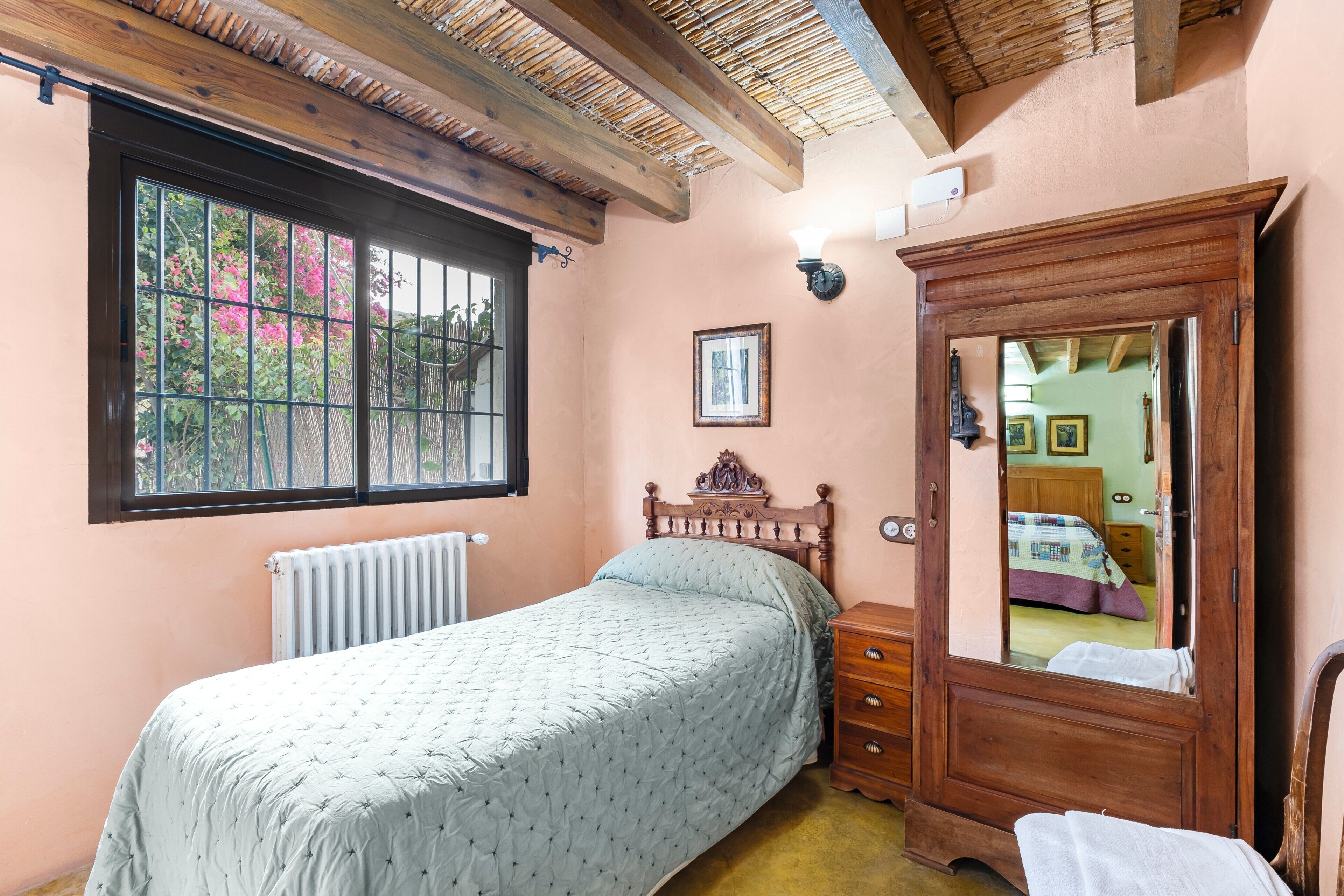 A bedroom with a bed, a dresser, a window with a view, and a wooden ceiling.