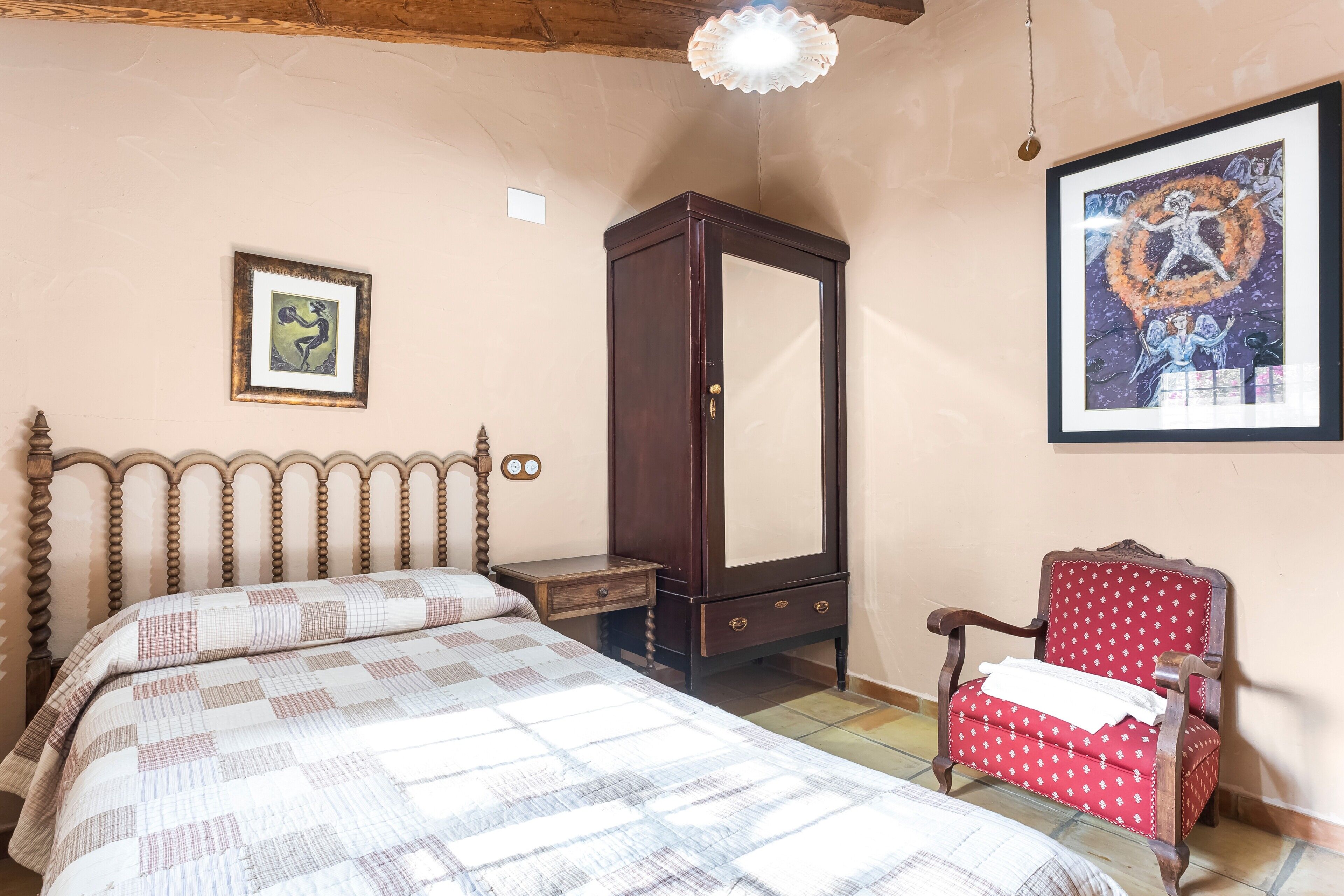 A bedroom with a bed, a wooden wardrobe, a red chair, and two framed pictures on the wall.