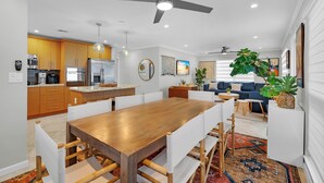 A modern kitchen with wooden cabinets, a stainless steel refrigerator, and a dining area with a wooden table and white chairs.