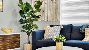 A modern living room with a dark blue sofa, a round wooden coffee table, and a large green plant.
