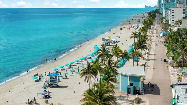 A beach with a lifeguard tower, umbrellas, and palm trees.