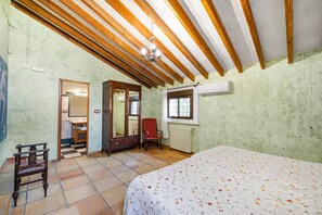 A bedroom with a bed, wooden ceiling beams, a radiator, a window, and a chair. - Country House 'La Carrasca - Naranja' with Shared Pool, Wi-Fi and Air Conditioning (Catral)