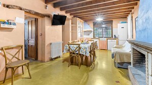 A dining area with a table set for four, wooden chairs, a television mounted on the wall, and a kitchen area with a refrigerator and sink. - Country House 'La Carrasca - Naranja' with Shared Pool, Wi-Fi and Air Conditioning (Catral)