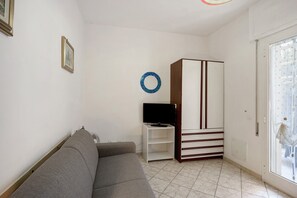 Una stanza con un divano grigio, una TV su un mobile bianco, un armadio e una porta con vetri smerigliati.