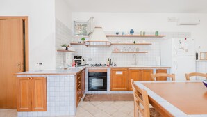 A modern kitchen with white tiles, wooden cabinets, a built-in oven, and a dining area with a wooden table and chairs. - Apartment 'Elena' with Mountain View, Wi-Fi and Air Conditioning (Alcamo)