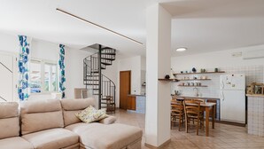 A modern living room with a sofa, a dining area with chairs, a kitchen with a refrigerator, and a spiral staircase. - Apartment 'Elena' with Mountain View, Wi-Fi and Air Conditioning (Alcamo)