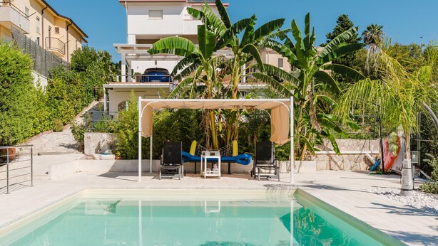 A pool area with a clear view of the surrounding buildings, a covered seating area, and a staircase leading to the buildings. - Apartment 'Elena' with Mountain View, Wi-Fi and Air Conditioning (Alcamo)