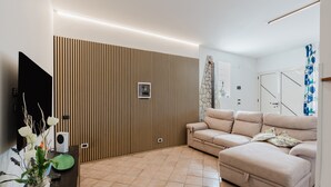 A modern living room with a sofa, a TV, a plant, and a wall with vertical lines. - Apartment 'Elena' with Mountain View, Wi-Fi and Air Conditioning (Alcamo)