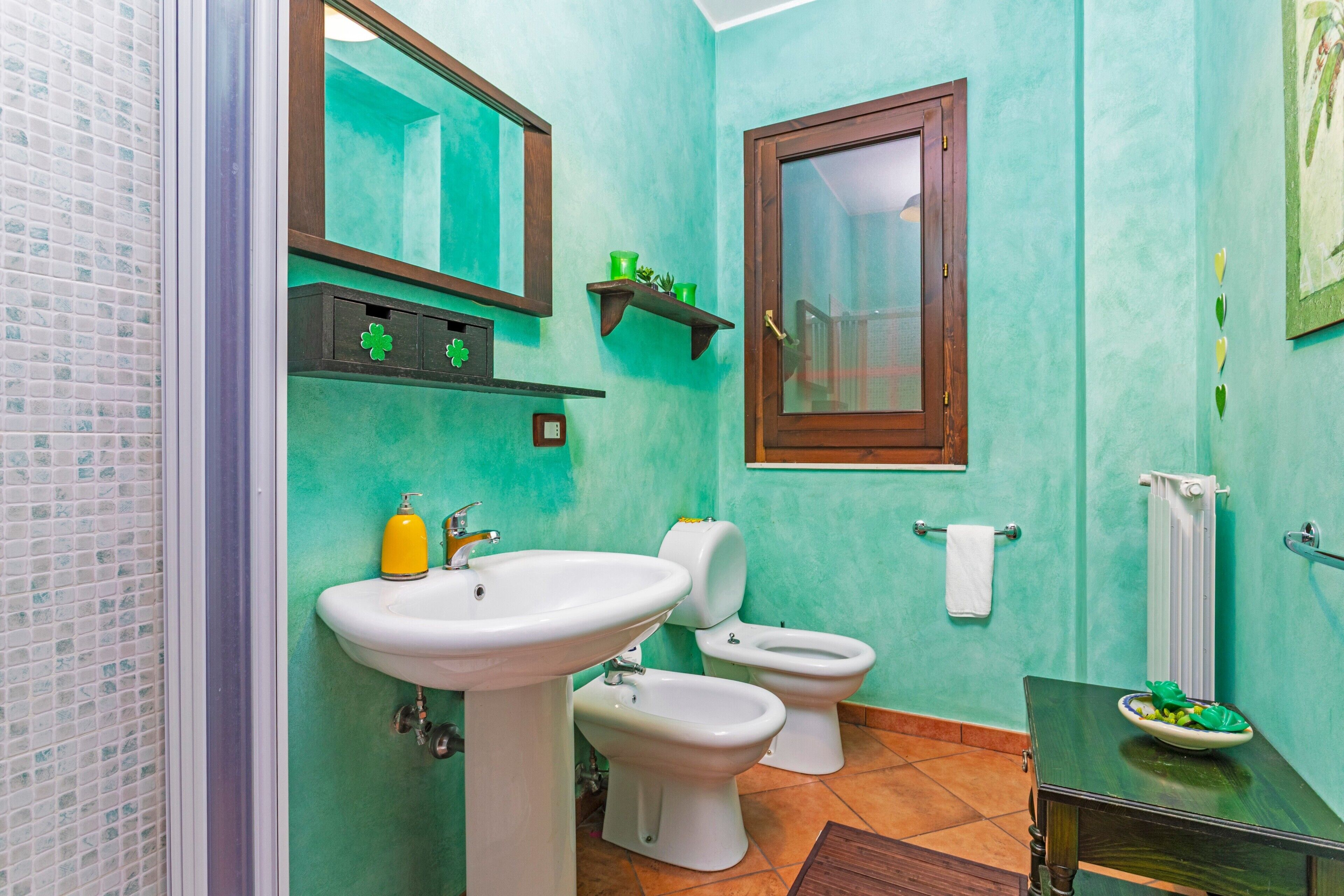 Une salle de bain avec un lavabo, deux toilettes, un miroir et une fenêtre.