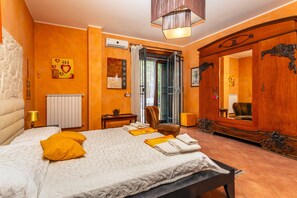 Quarto de hotel com cama, uma cadeira, guarda-roupa de madeira, espelho e janela com cortinas.