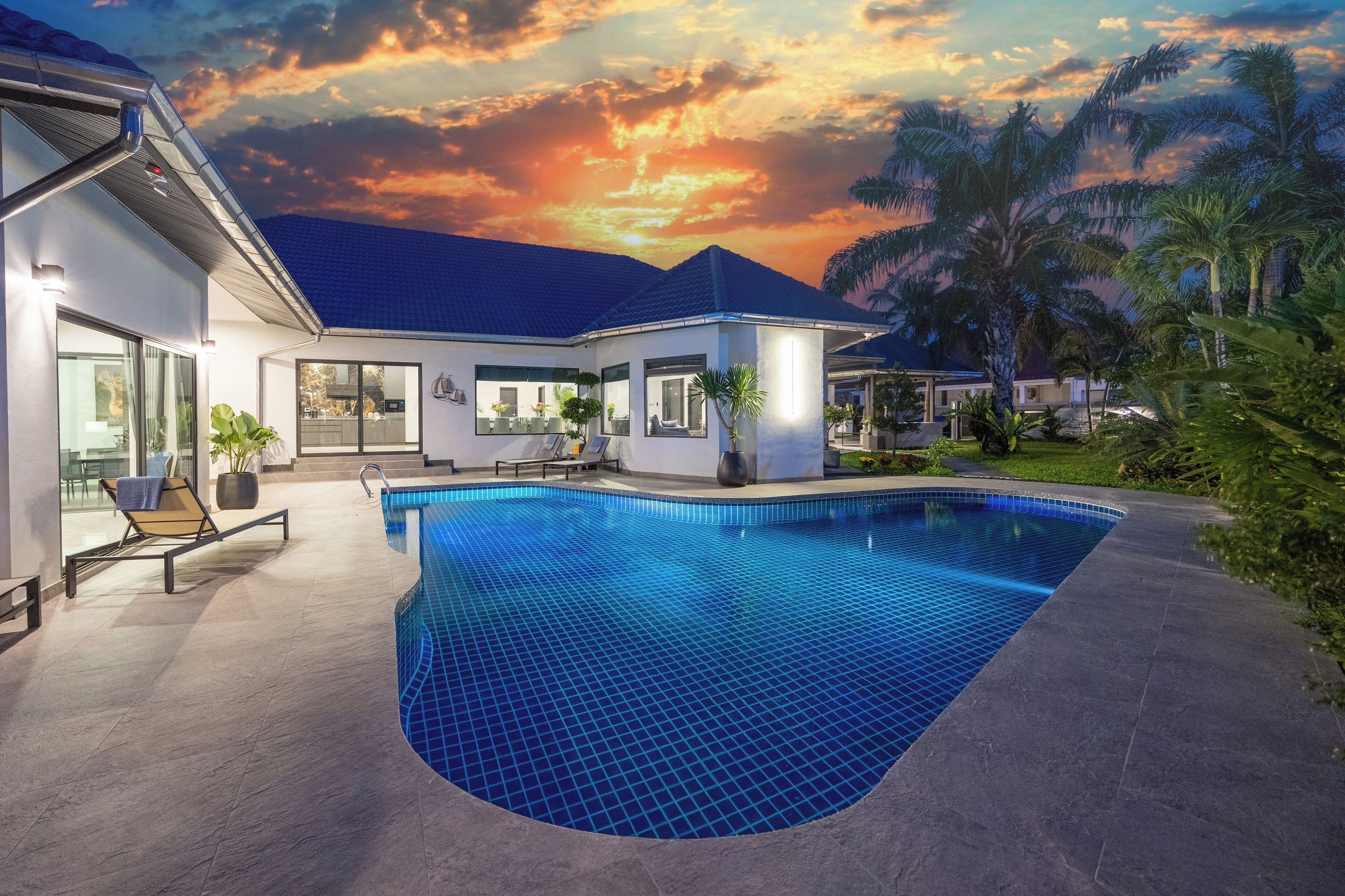 A modern house with a swimming pool, large windows, and a view of the sunset.