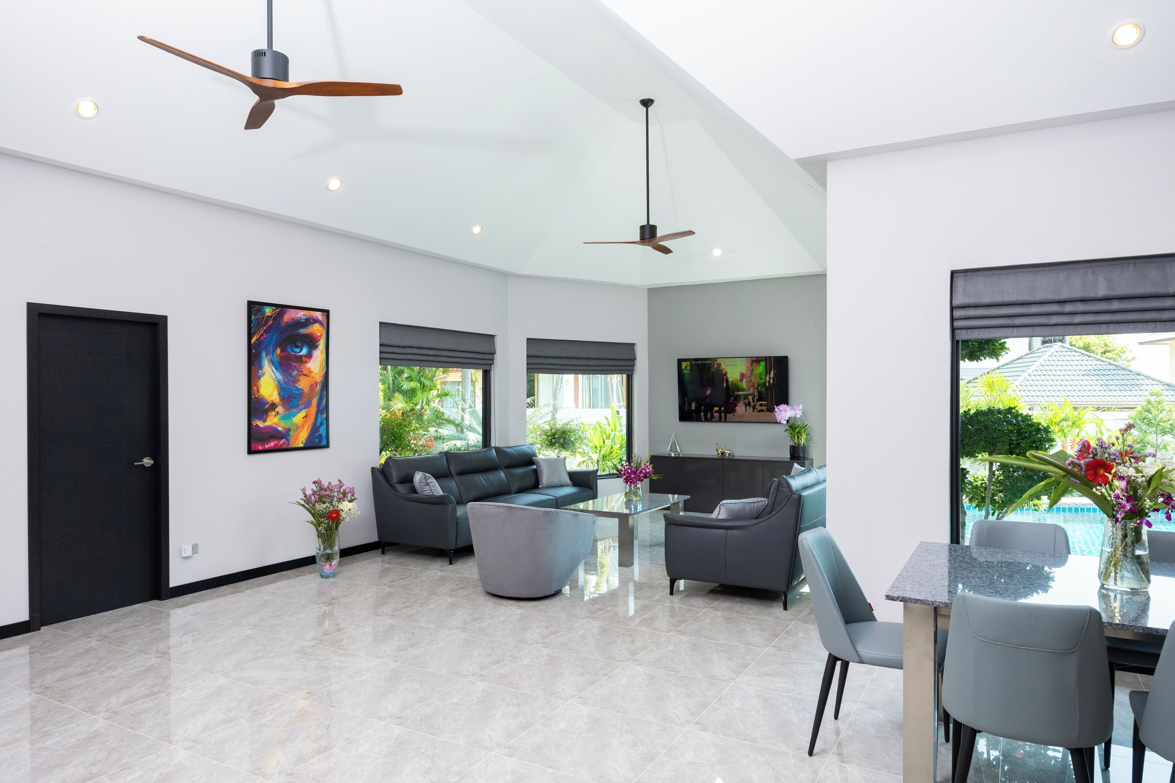 A spacious living area with a modern design, featuring a large sofa set, a dining table, and a ceiling fan.