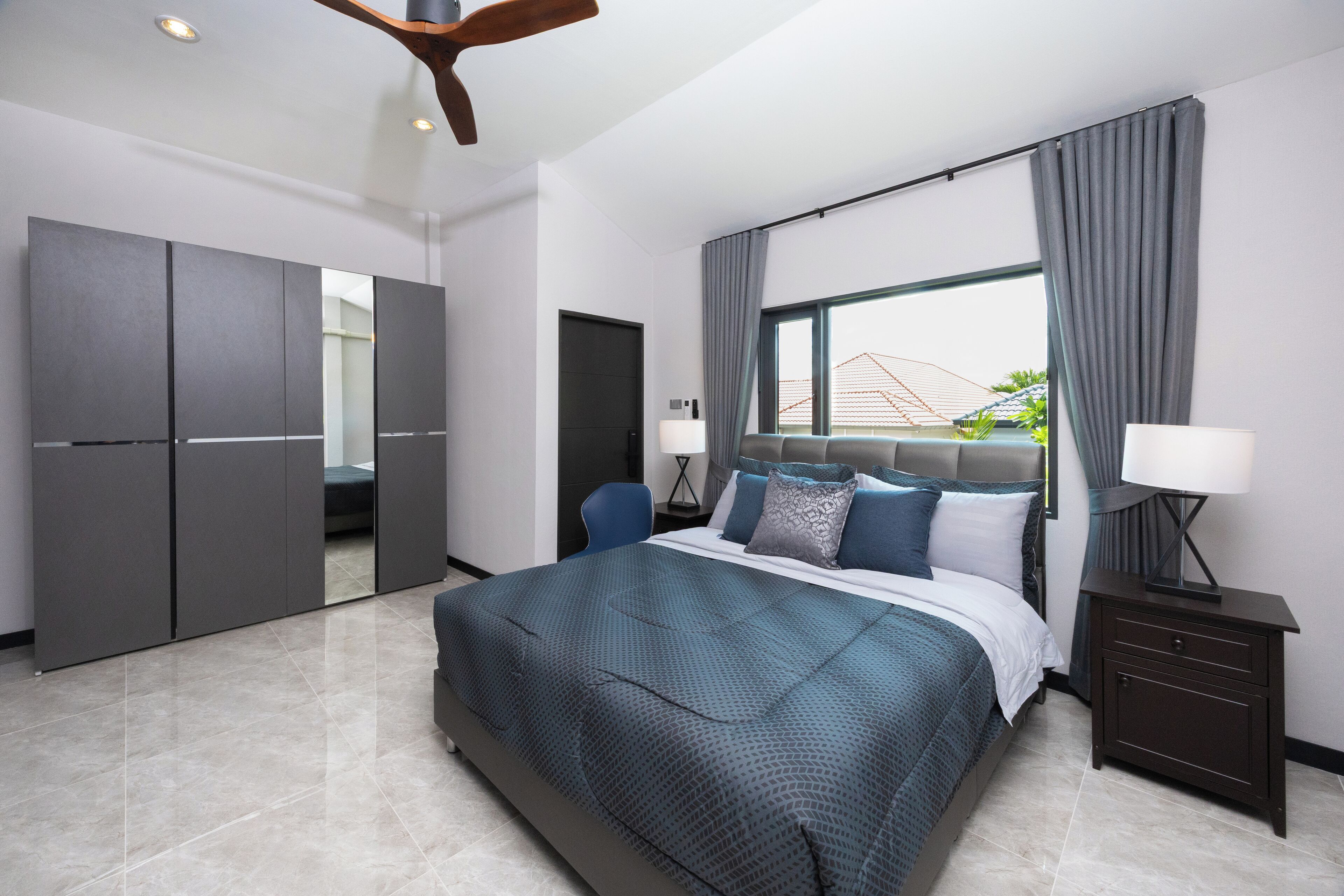 A modern bedroom with a large bed, a wardrobe, a desk, and a window with curtains.