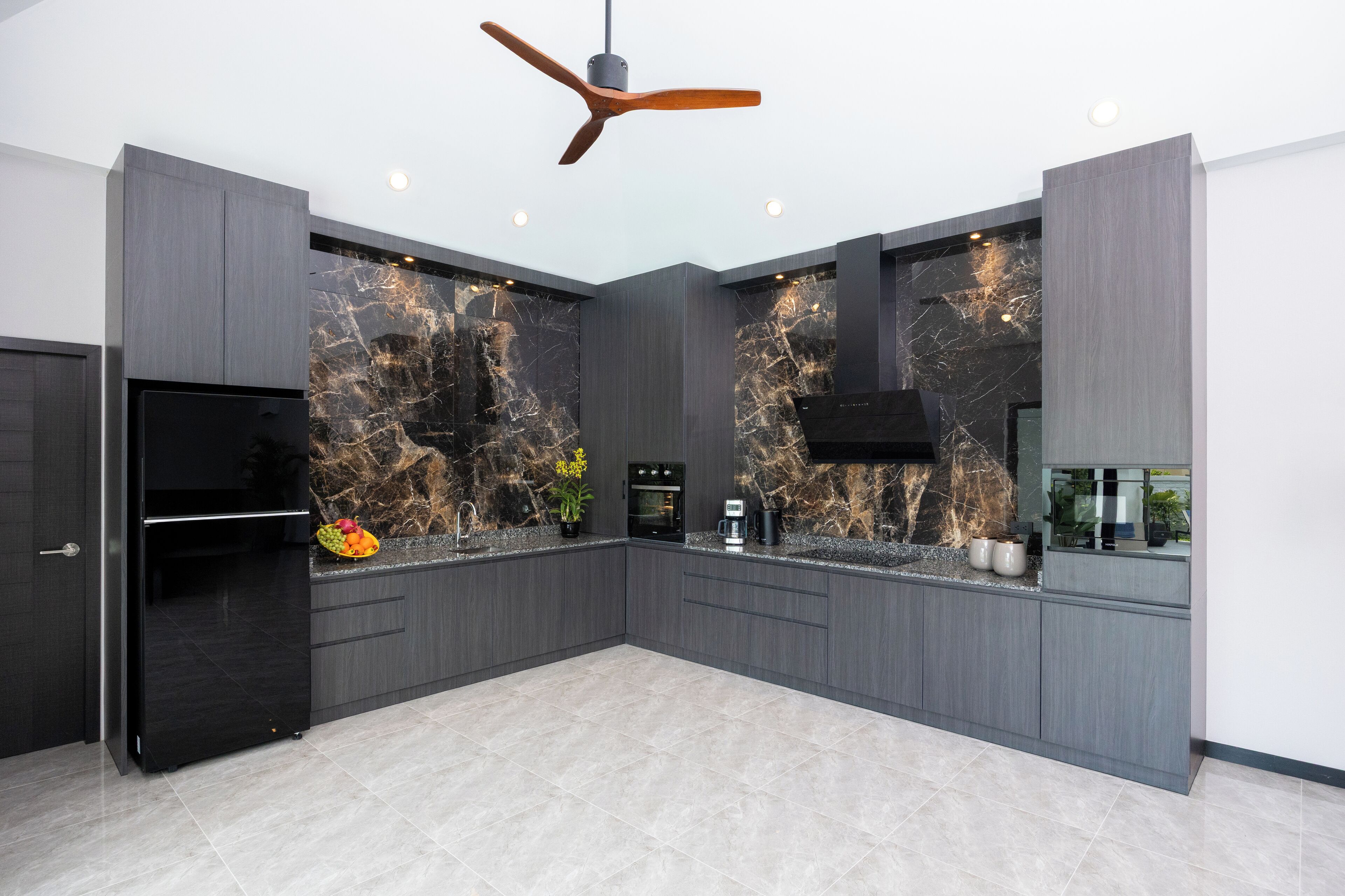 A modern kitchen with dark cabinetry, a black refrigerator, and a marble backsplash.