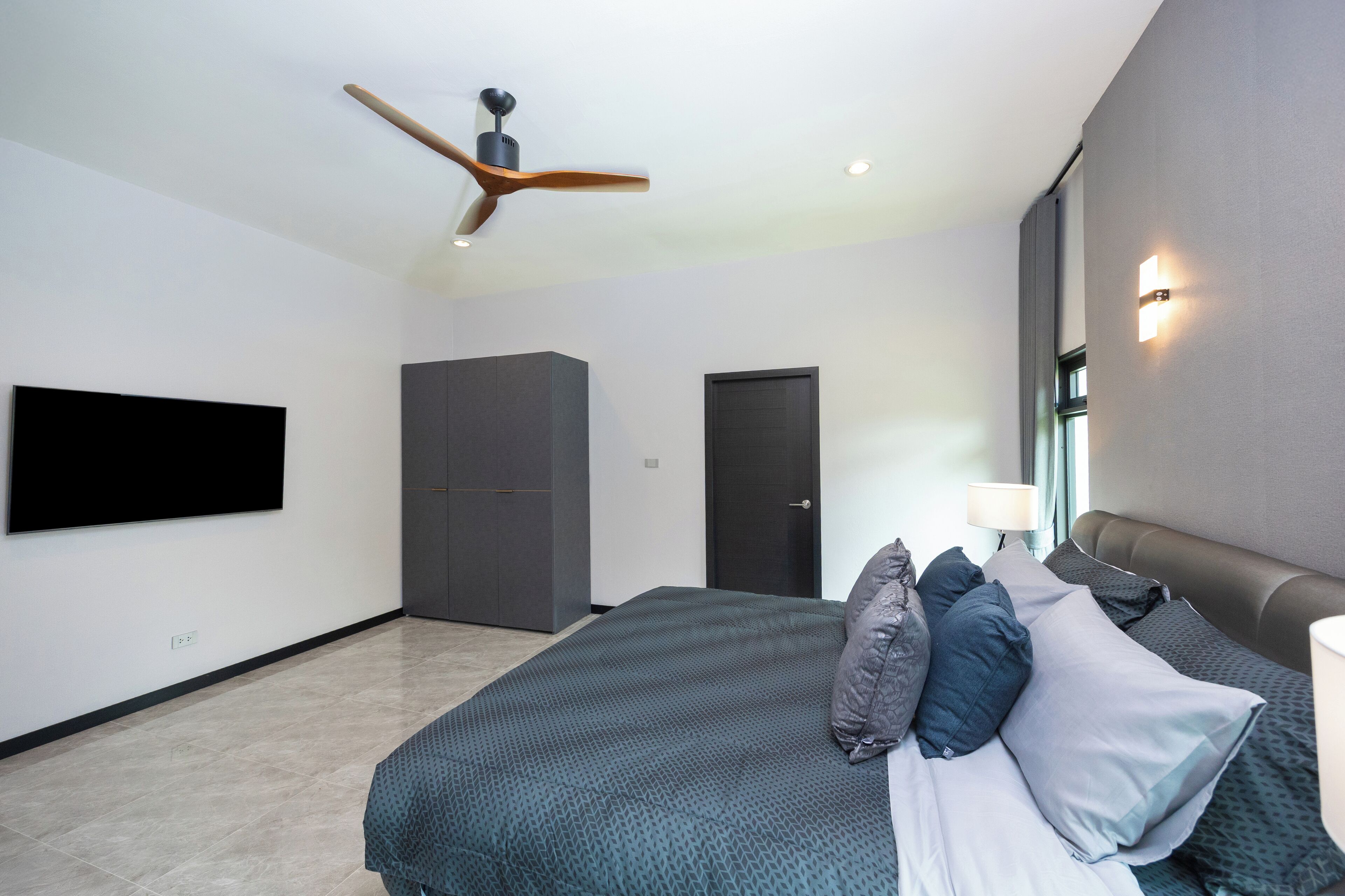 A modern bedroom with a large bed, a ceiling fan, a flat-screen TV, and a wardrobe.