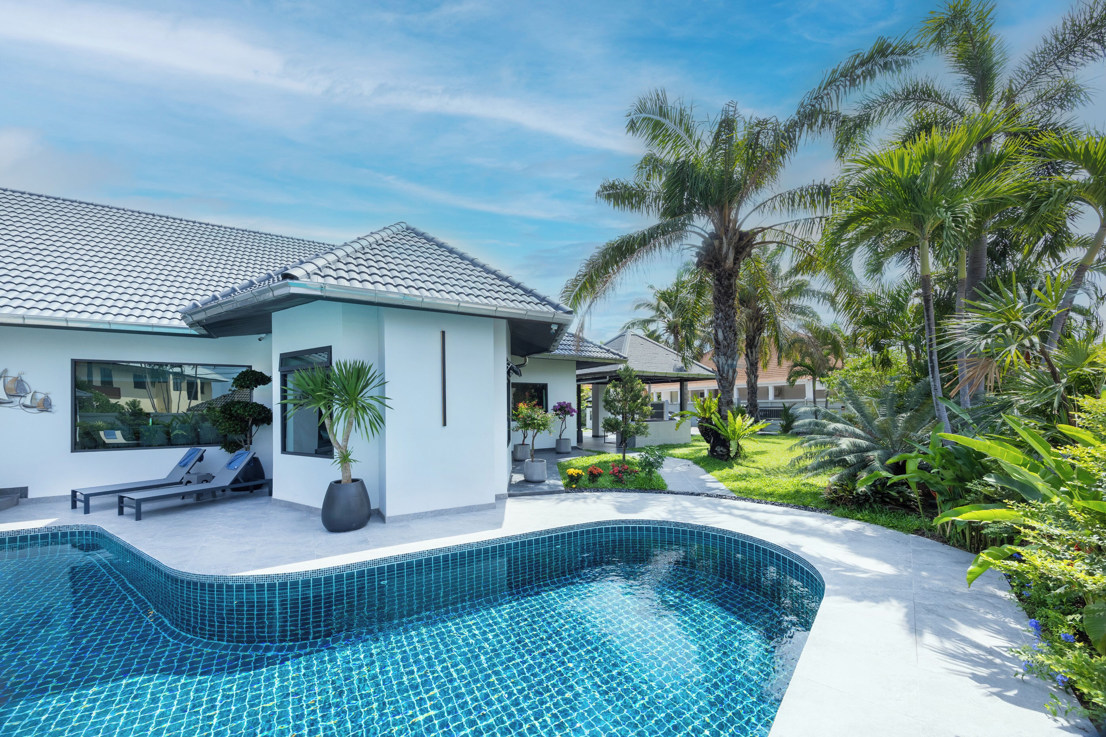 A modern house with a swimming pool, a lounge area, and a garden with palm trees.