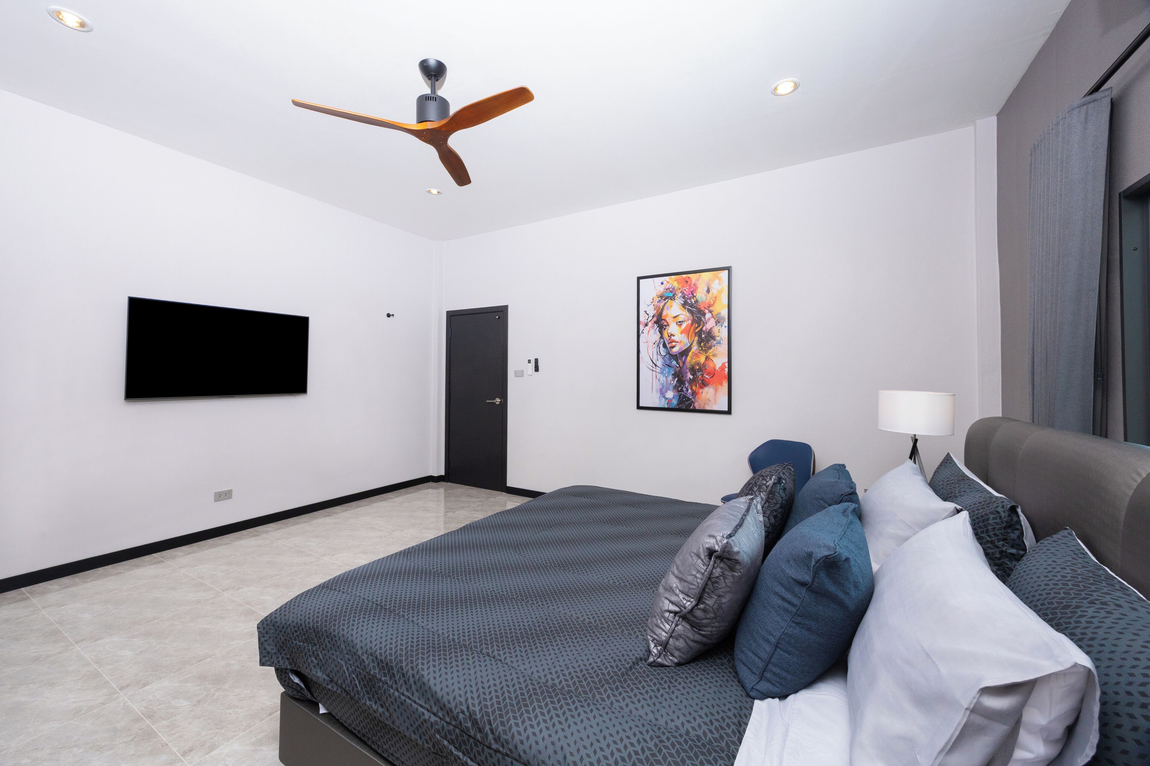A modern bedroom with a bed, pillows, a ceiling fan, a flat-screen TV, and a door.