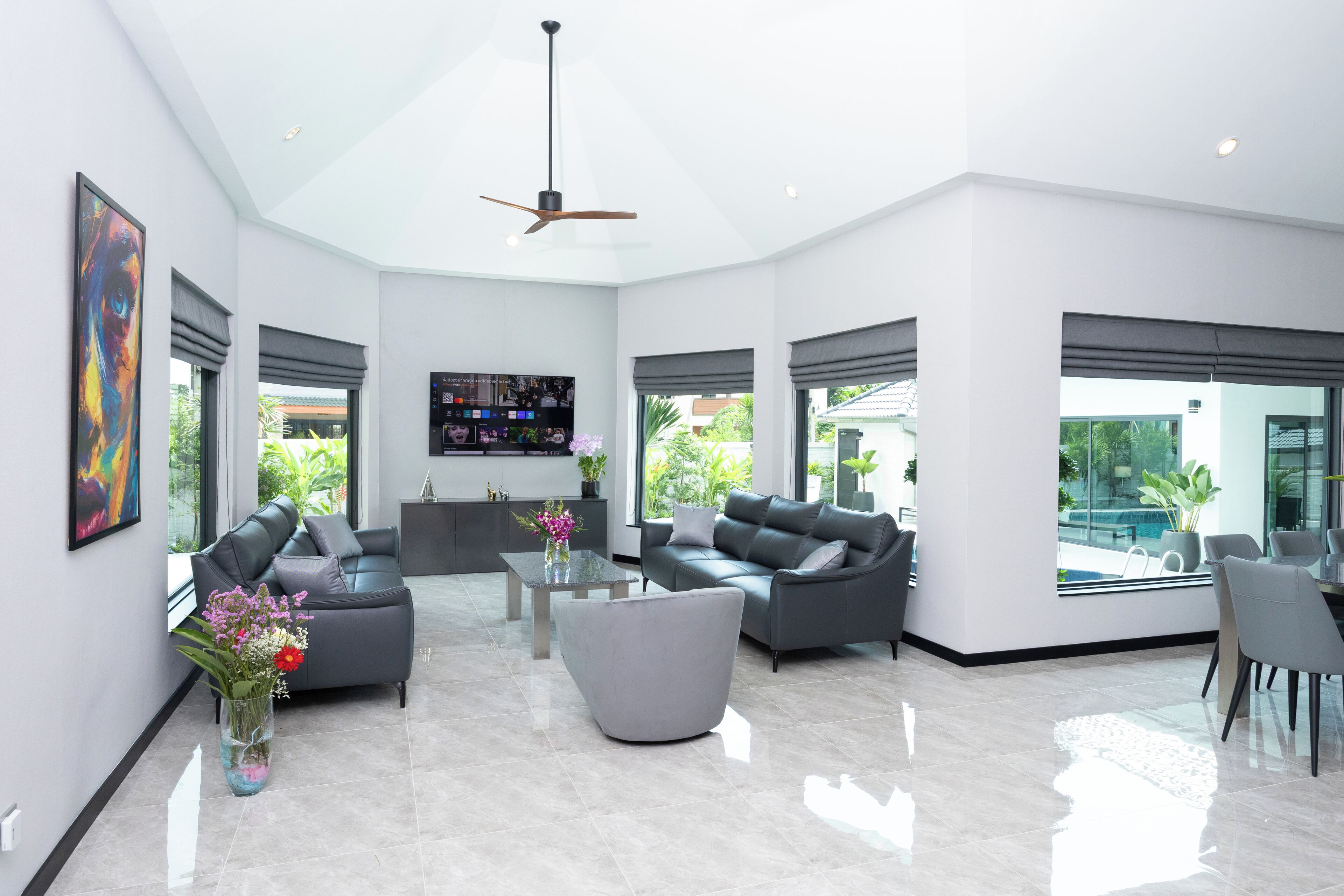 A spacious living room with a modern design, featuring a large grey sofa, a glass coffee table, and a ceiling fan.
