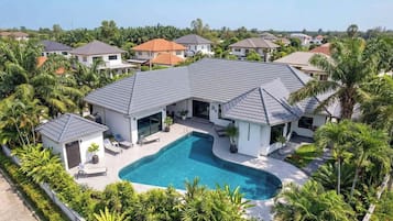 A residential property with a swimming pool, surrounded by lush greenery and palm trees.