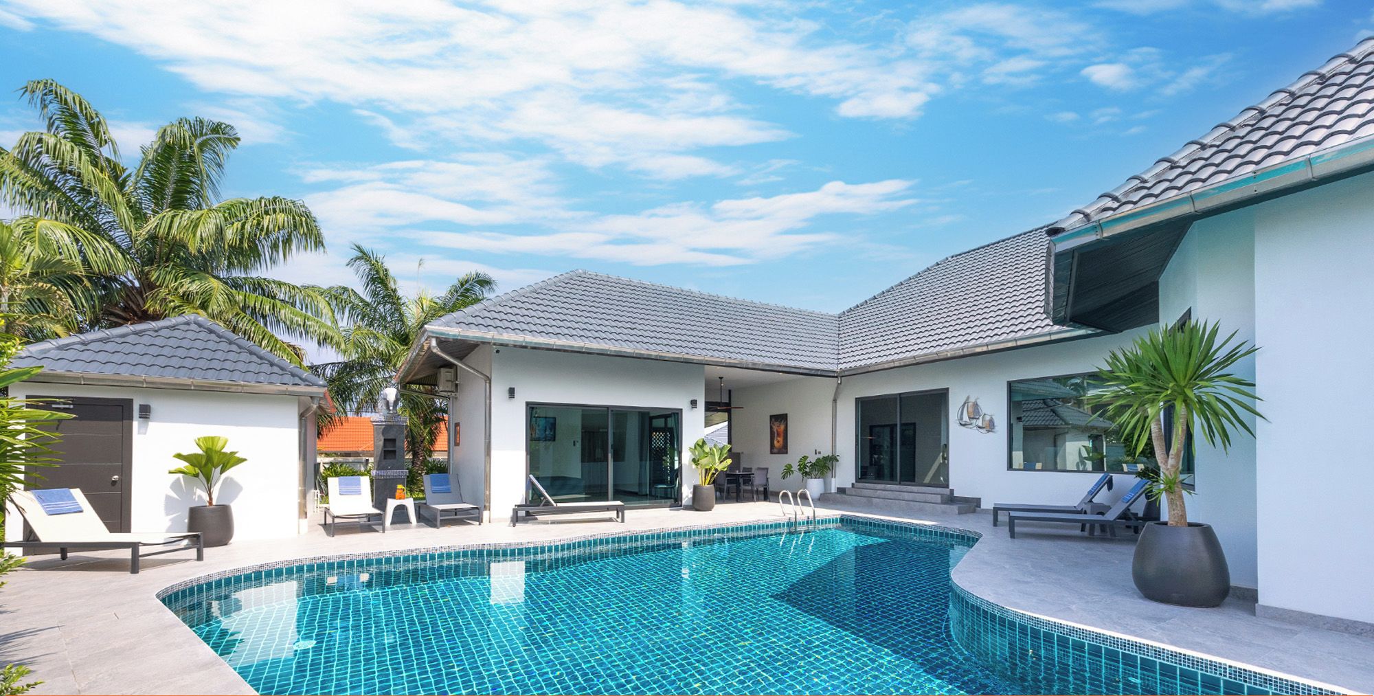 A modern house with a swimming pool, lounge chairs, and a covered patio area.