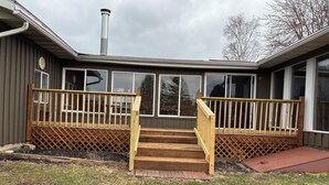 A residential building with a wooden deck, a chimney, and a large windowed porch.