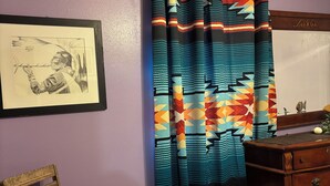 A room with purple walls, a wooden chair with a cushion, a wooden dresser, and a colorful curtain.