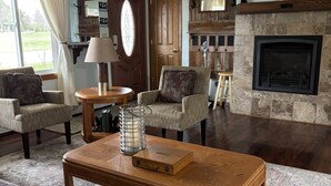 A spacious living room with a fireplace, two armchairs, a sofa, a coffee table, and a ceiling fan. - Wheelchair assessable spacious 5-bedroom house in Algoma (Algoma)