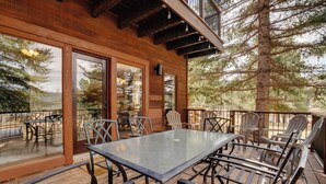 Una terraza de madera con un porche acristalado, mobiliario exterior y vistas a árboles.