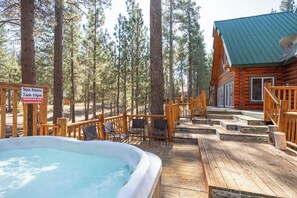 A wooden cabin with a hot tub, outdoor seating, and a sign indicating spa hours.