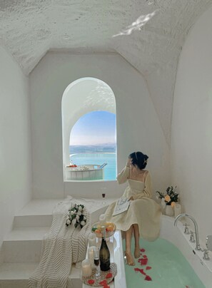 A room with a bathtub, a window with a view of the sea, a table with a bottle and candles, and a chair with a blanket. - Man hai Valley Homestay (Ningde)