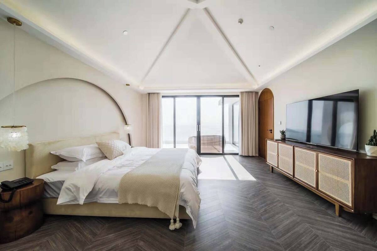A modern bedroom with a large bed, a TV, and a sliding glass door to a balcony.