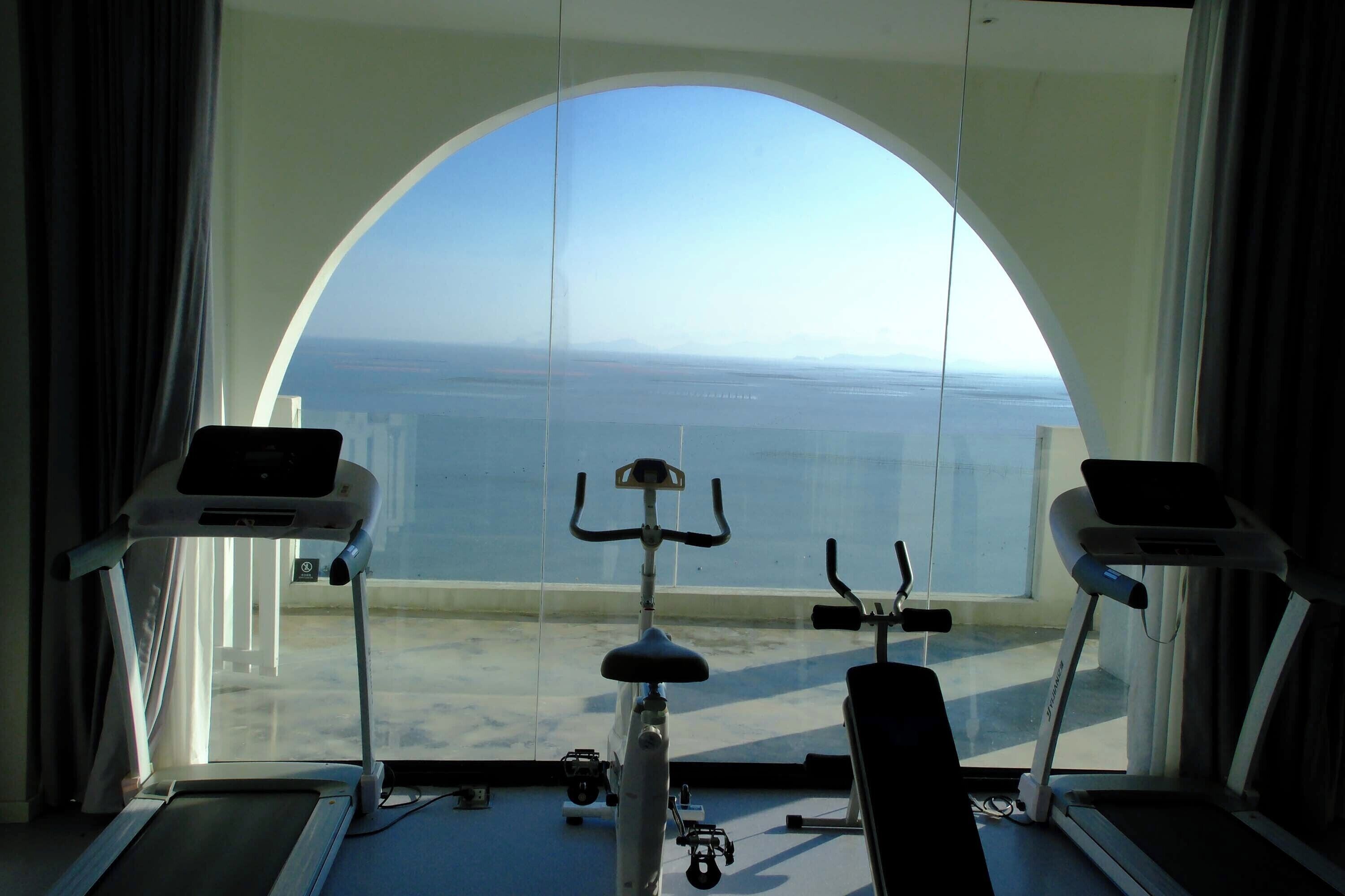 A gym with exercise equipment and a large arched window overlooking a body of water.
