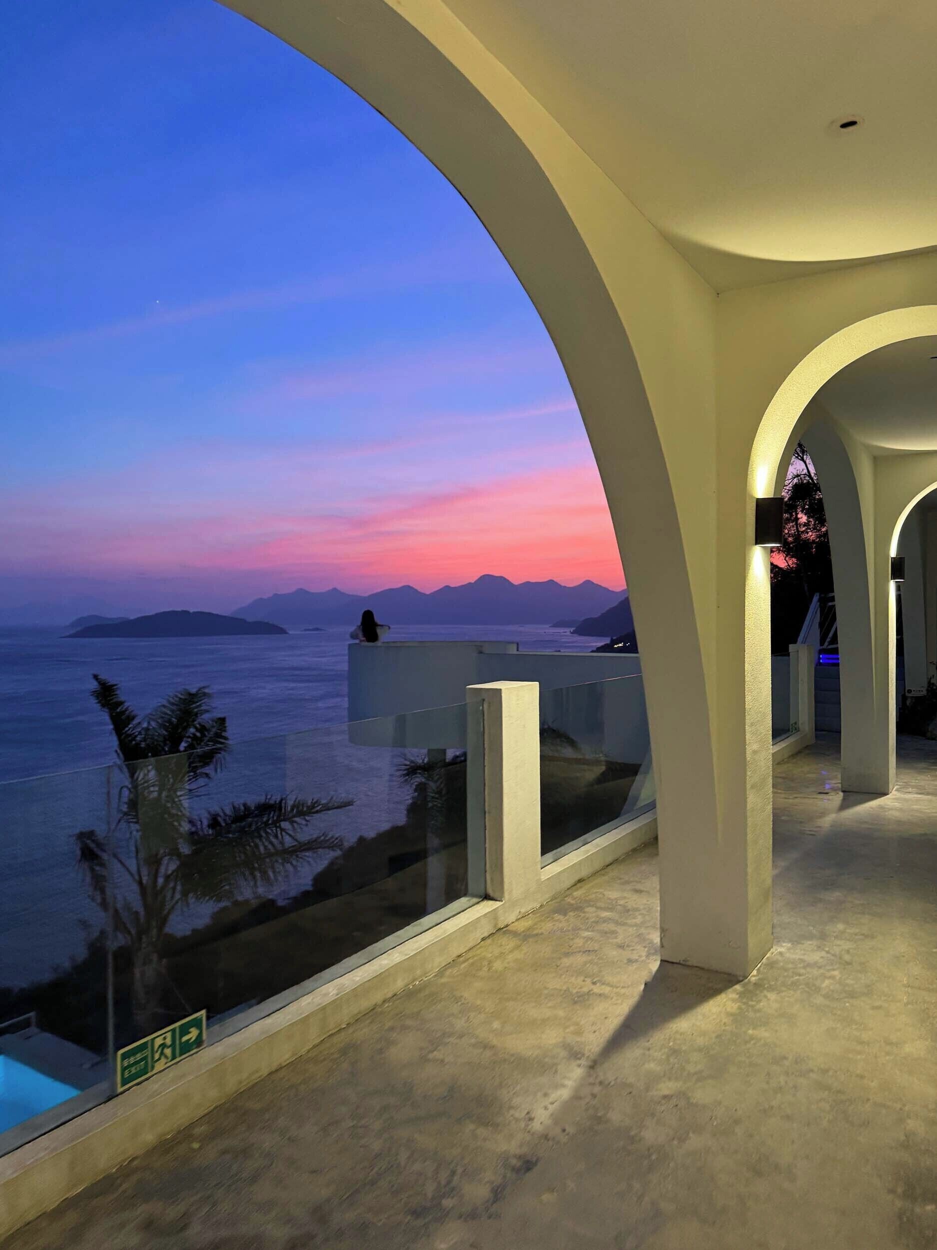 Ein Balkon mit Blick auf das Meer und die Berge im Abendrot.