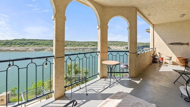 Un balcon offrant une vue sur une rivière et des collines, avec une table, des chaises et une petite table sur laquelle est posé un objet décoratif.