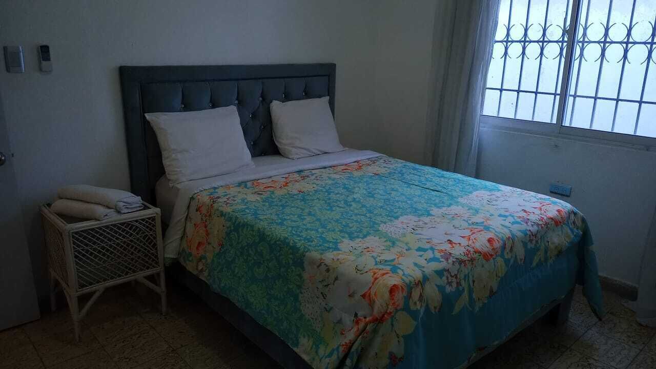 Een slaapkamer met een bed, een nachtkastje en een raam met tralies.