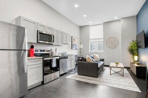 A modern kitchen with stainless steel appliances, a grey sofa, and a flat-screen TV.