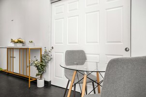 A room with a glass table, a grey chair, a small potted plant, and a white door.